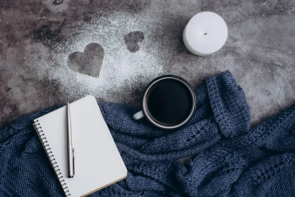 Cup of coffee , candle, notebook, pen and warm woolen sweater  on gray table.Winter concept. Flat lay, top view. Valentines day.