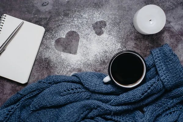 Cup of coffee , candle, notebook, pen and warm woolen sweater  on gray table.Winter concept. Flat lay, top view. Valentines day.