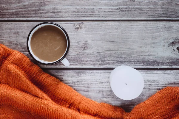 Winter cozy concept. Flat lay of orange knitted sweater, candle and coffee with milk  on wooden table