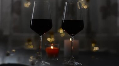 İki kadeh şarap kırmızı duran mum ve çelenk karanlık bir tablo