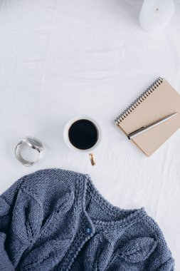 Fincan kahve, mavi örgü kazak, defter kalem, saat, mum ile yatak, en iyi görünüm. Kadın giyim. Düz yatıyordu, rahat kavramı