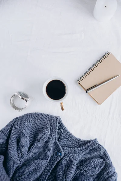 Fincan kahve, mavi örgü kazak, defter kalem, saat, mum ile yatak, en iyi görünüm. Kadın giyim. Düz yatıyordu, rahat kavramı