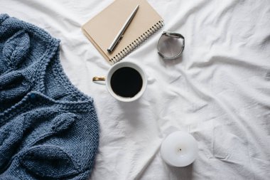 Fincan kahve, mavi örgü kazak, defter kalem, saat, mum ile yatak, en iyi görünüm. Kadın giyim. Düz yatıyordu, rahat kavramı