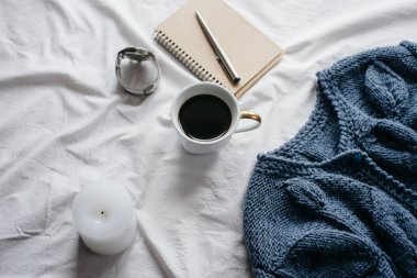 Fincan kahve, mavi örgü kazak, defter kalem, saat, mum ile yatak, en iyi görünüm. Kadın giyim. Düz yatıyordu, rahat kavramı