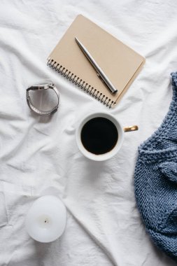 Fincan kahve, mavi örgü kazak, defter kalem, saat, mum ile yatak, en iyi görünüm. Kadın giyim. Düz yatıyordu, rahat kavramı
