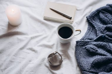 Fincan kahve, mavi örgü kazak, defter kalem, saat, mum ile yatak, en iyi görünüm. Kadın giyim. Düz yatıyordu, rahat kavramı