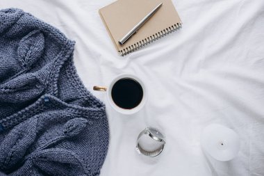 Fincan kahve, mavi örgü kazak, defter kalem, saat, mum ile yatak, en iyi görünüm. Kadın giyim. Düz yatıyordu, rahat kavramı