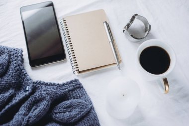 Mavi örgü kazak, kahve, defter, mum, yatakta, üstten görünüm akıllı telefon. Kadın giyim. Düz yatıyordu, rahat kavramı