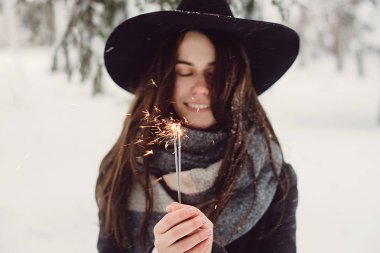 Şapkalı mutlu ve gülümseyen kız sokakta kar yağışı sırasında Bengal ışık tutar. Kış konsepti