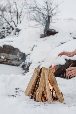 Kamp ateşi ellerine ısınma erkek bir kış döneminde kar karşı çevrili yakınındaki donmuş gölün. Kavramı macera aktif tatiller spor hiking açık 