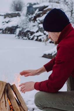 Kamp ateşi ellerine ısınma erkek bir kış döneminde kar karşı çevrili yakınındaki donmuş gölün. Kavramı macera aktif tatiller spor hiking açık 