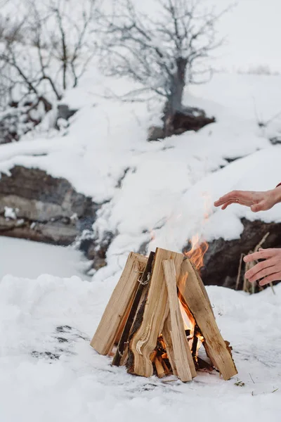 Kamp ateşi ellerine ısınma erkek bir kış döneminde kar karşı çevrili yakınındaki donmuş gölün. Kavramı macera aktif tatiller spor hiking açık 