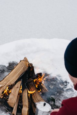 Kamp ateşi ellerine ısınma erkek bir kış döneminde kar karşı çevrili yakınındaki donmuş gölün. Kavramı macera aktif tatiller spor hiking açık 