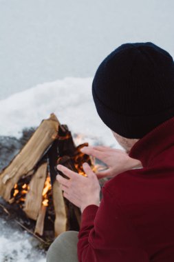 Kamp ateşi ellerine ısınma erkek bir kış döneminde kar karşı çevrili yakınındaki donmuş gölün. Kavramı macera aktif tatiller spor hiking açık 