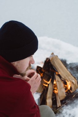 Kamp ateşi ellerine ısınma erkek bir kış döneminde kar karşı çevrili yakınındaki donmuş gölün. Kavramı macera aktif tatiller spor hiking açık 