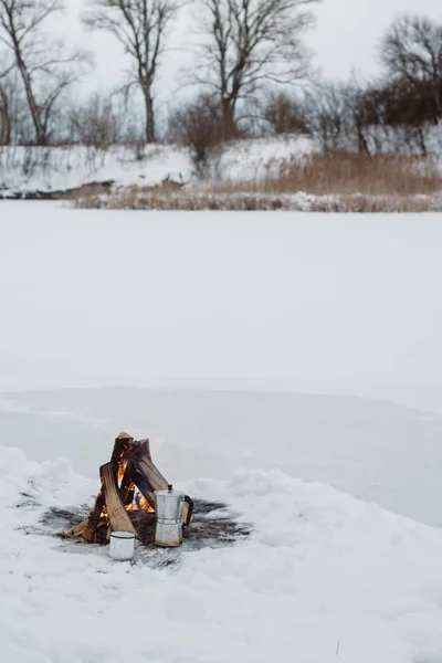 up of coffee and a coffee maker on the background Camp fire an in winter time, surrounded by snow against the near of the frozen lake. Concept adventure active vacations outdoor hiking sport