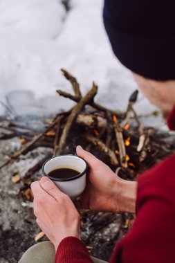 Turistik bir fincan sıcak kahve ile kamp ateşi oturan bir kış zamanında. Kavramı macera aktif tatiller açık. Kış kamp