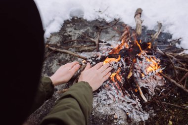 Şapkalı kız ellerini yangın yanında kışın sıcak. Kavramı macera aktif tatiller açık. Kış kamp
