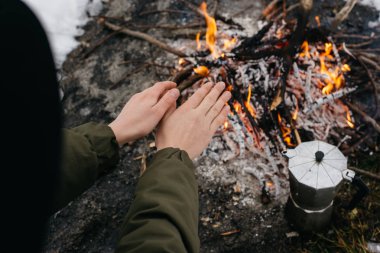Şapkalı kız ellerini yangın yanında kışın sıcak. Kavramı macera aktif tatiller açık. Kış kamp