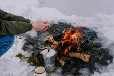  Kız kahve bir ateş yakın elleriyle kışın sıcak. Kavramı macera aktif tatiller açık. Kış kamp