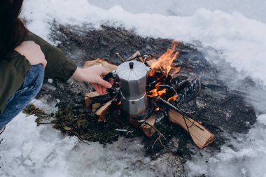 Kadın oturur camp yakınındaki ateş ve kışın açık pişirme kahvesidir. Kavramı macera aktif tatiller. Kış kamp