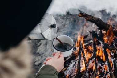 Seyahat-kadın oturur camp yakınındaki bir ateş içinde bir kış zaman ve kendisi sıcak kahve dökülen. Kavramı macera aktif tatiller açık. Kış kamp