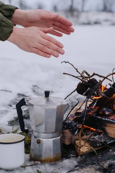 Girl  warms hands with coffee near a fire in winter. Concept adventure active vacations outdoor. Winter camping