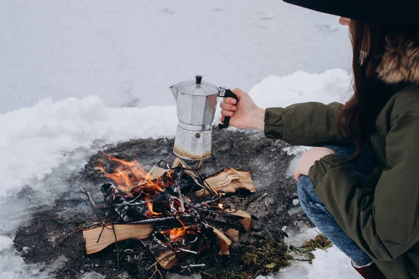 Woman  a  sits near camp fire and is cooking coffee in the outdoor in the winter . Concept adventure active vacations . Winter camping