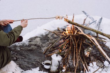 Kar karşı çevrili kamp ateşi üzerinde Marshmallows kavurma kız yakınındaki donmuş gölün. Kavramı macera aktif tatiller açık. Kış Kampı