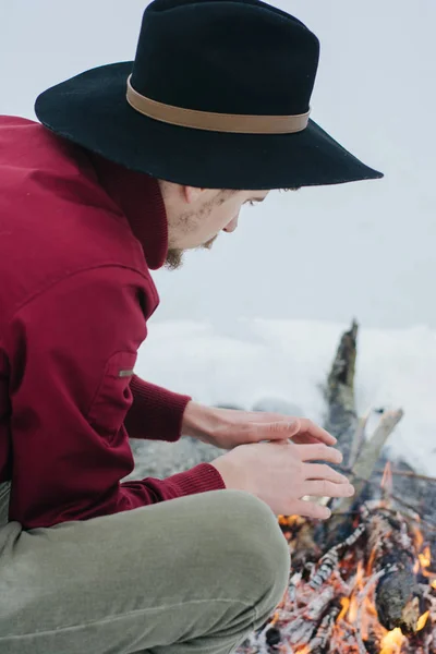 Winter camp. Tourist  in  hat warms hands near a fire in winter time. Concept adventure active vacations outdoor.