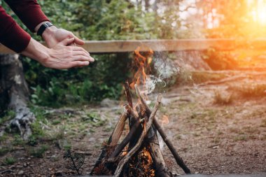 Yaz kampı. Adam bir kamp ateşi yakınındaki ormanda günbatımı zaman eller. Kavramı macera aktif tatiller açık.