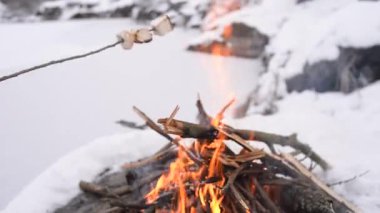Kar karşı çevrili kamp ateşi üzerinde Marshmallows kavurma kız yakınındaki donmuş gölün. Kavramı macera aktif tatiller açık. Kış Kampı