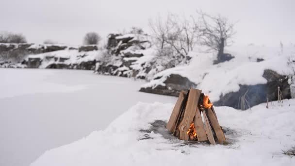 キャンプ火災の冬時間 凍った湖の背景に雪に囲まれています 概念冒険のアクティブな休暇の屋外スポーツをハイキング — ストック動画