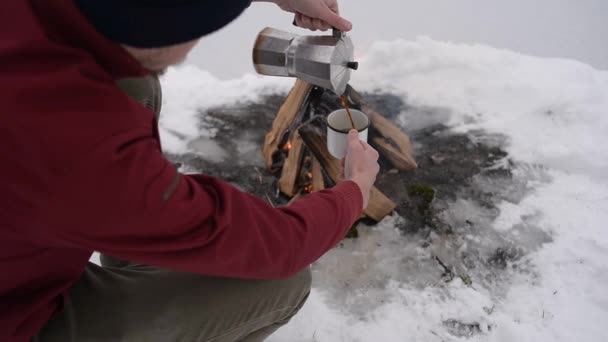 キャンプの近くに座る男の旅冬の火災時間および自体にホット コーヒーを注ぐ 概念冒険アクティブな休暇屋外 冬のキャンプ — ストック動画