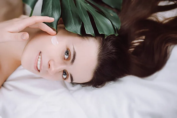 Menina Cabelos Longos Feliz Atraente Aplicando Creme Seu Rosto Deitado — Fotografia de Stock