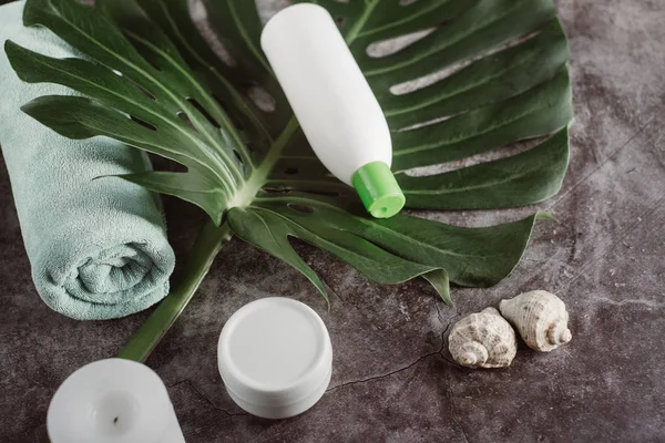 Flat lay composition with white cosmetic products, candle, towel and  green leaf on gray concrete background. Natural beauty products for skin care. Beauty concept and health. Place for text