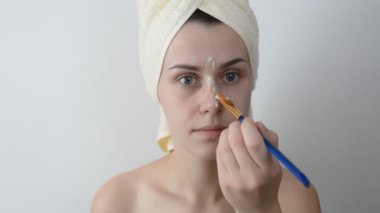 Yüzünü bir fırça sonra bir duş ile krem uygulayarak banyo havlusu ile sarılmış çekici genç kadın. Cilt bakım ve güzellik kavramı. Kadın yüzüne evde yüz maskesi uygulama.