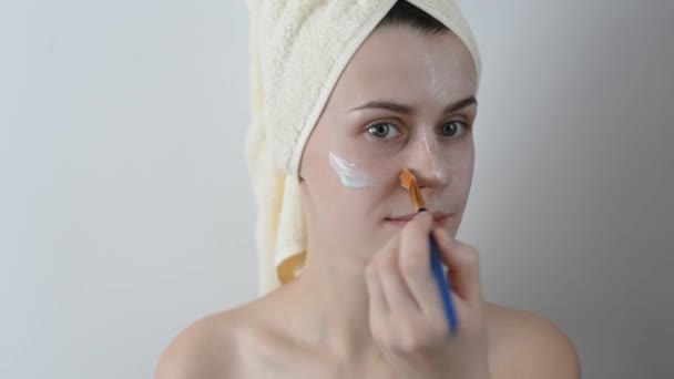 有吸引力的年轻女子包裹浴巾 在她的脸上涂上奶油与刷子淋浴后 护肤和美容理念 在家中的女性脸上涂面膜 — 图库视频影像