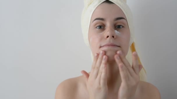 有吸引力的年轻女孩包裹着浴巾 在她的脸上涂上奶油淋浴后 护肤和美容概念 — 图库视频影像