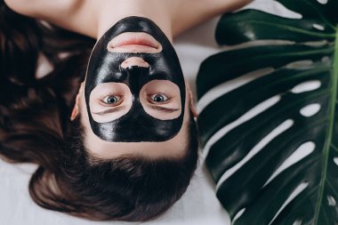 Çekici kızı aç gözlerini ve yatakta yatan yaprak yeşil siyah bir maske yüzüne karşı uygulanır. Kadın siyah bir yüz maskesi ile rahatlatıcı. Kavram sağlık ve güzellik . 