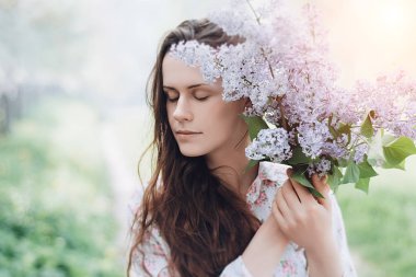 Güzel kız parkta mor çiçekler bir yaz günü, leylak Bush tutar. Bahar güneşin doğada bir kız portresi. Bahar kavramı. seçici odak