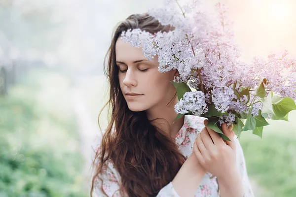 Güzel kız parkta mor çiçekler bir yaz günü, leylak Bush tutar. Bahar güneşin doğada bir kız portresi. Bahar kavramı. seçici odak