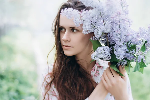 Güzel kız parkta mor çiçekler bir yaz günü, leylak Bush tutar. Bahar güneşin doğada bir kız portresi. Bahar kavramı. seçici odak
