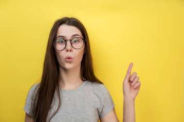 Sürpriz beyaz genç bayan gri T-shirt, sarı arka plana karşı modelleri giyinmiş nefes nefese, boş kopya alanı reklam için bir şey gösterir.