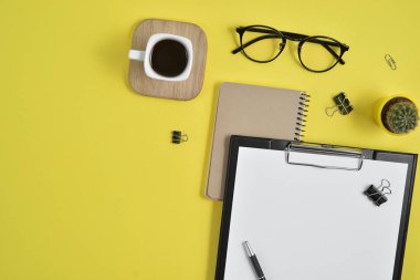 Düz yatıyordu, en iyi görünümü office tablo Resepsiyon. Çalışma alanı boş klibi kurulu, büro malzemeleri, kalem, kaktüs, Sarı zemin üzerine kahve Kupası ve göz gözlük ile. Blog kavramı