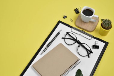 Ofis Resepsiyon çalışma alanı boş klibi kurulu, büro malzemeleri, kalem, kaktüs, yaprak yeşil, kahve fincanı bir ahşap stand ve Sarı zemin üzerine gözlük ile. Düz yatıyordu, en iyi görünümü blog kavramı