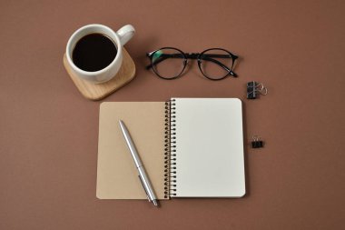 Ofis, banka donatımı, kalem, kahve fincanı, not defteri ve kahverengi zemin üzerine gözlük ile mockup çalışma alanı. Düz yatıyordu, en iyi görünüm, kopya alanı