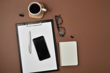Düz yatıyordu, en iyi görünümü office tablo Resepsiyon. Çalışma alanı boş klibi kurulu, defter, ofis, banka donatımı, gözlük, kalem, cep telefonu ve kahve fincanı kahverengi zemin üzerine