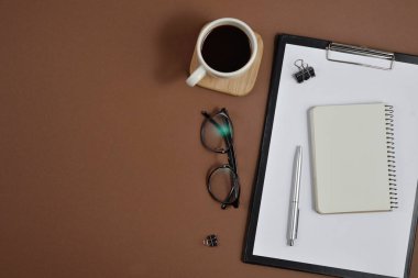 Çalışma alanı boş klibi kurulu, büro malzemeleri, kalem, kahve fincanı, not defteri ve kahverengi zemin üzerine gözlük ile alay. Düz yatıyordu, en iyi görünüm, kopya alanı
