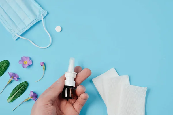 Concepto creativo plano de la alergia estacional al polen de primavera y verano con servilletas, pastillas, mascarilla facial, botella de gotas en mano masculina y flores sobre fondo azul. Vista superior, espacio de copia, estilo mínimo — Foto de Stock